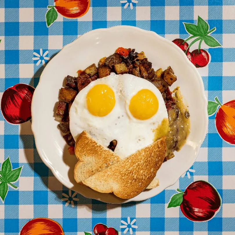 Doo-Dah Diner's breakfast plate with two fried eggs, hash, gravy, and toast on a checkered tablecloth.